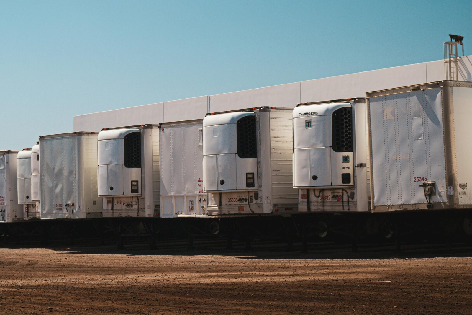 Refrigerated trucks parked in an industrial lot under a clear blue sky on a sunny day.